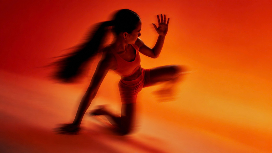 Motion-blurred athlete sprinting out of a crouch against a glowing orange background
